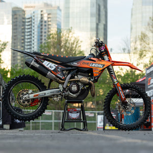 Orange and black dirt bike on a Risk Racing MX stand with cityscape in the background