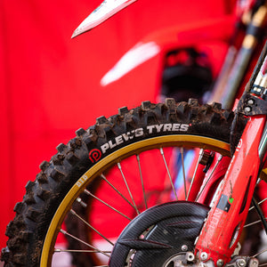 Close up of a motocross bike's front tire and front forks. Plews Tyres logo on the side of the front tire.