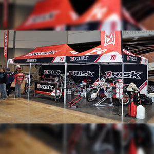 A 10x10 and 10x20 canopy pit tent with tent walls installed on the back wall of both. Showroom floor setting at a trade show.