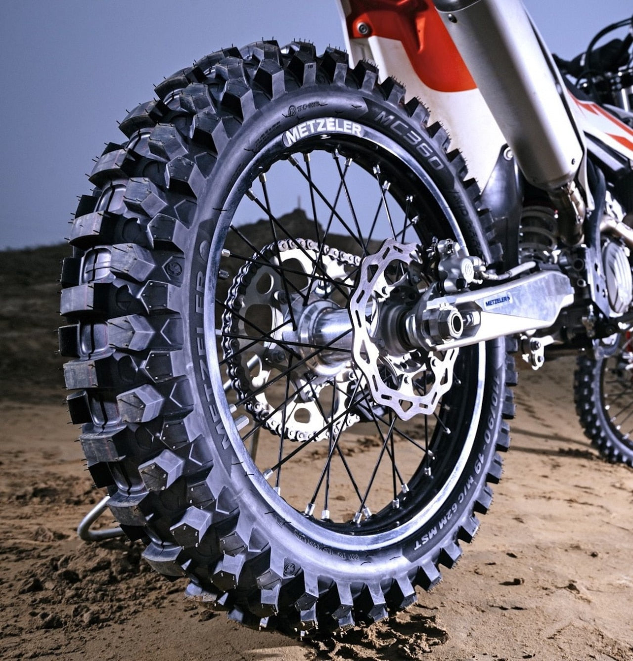 Dirt bike tire on a ktm dirt bike. it appears to be a brand new offroad tire with deep aggressive nobbies for conquering off-road terrain