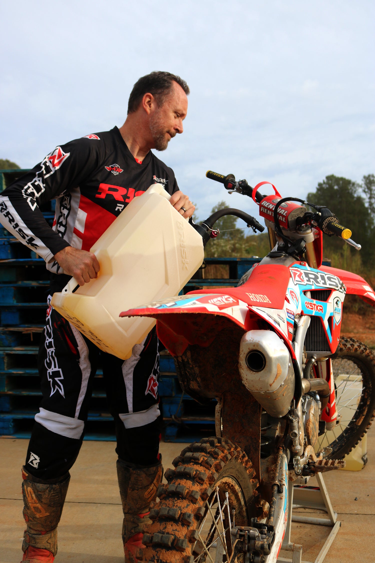 MX rider fueling up his dirt bike with an EZ Utility Jug. He's wearing the mix n match V2 pants and black n red jersey