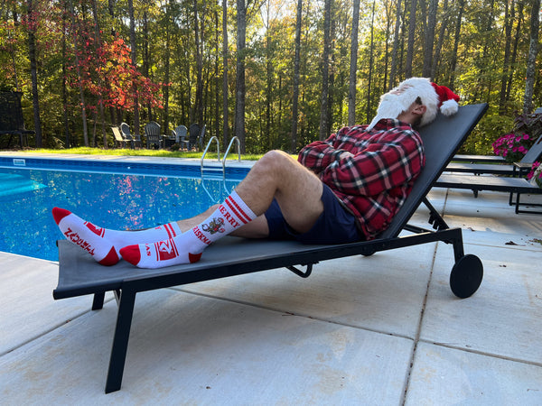 Santa wearing Riskmas socks laying poolside arms folded head back chillin