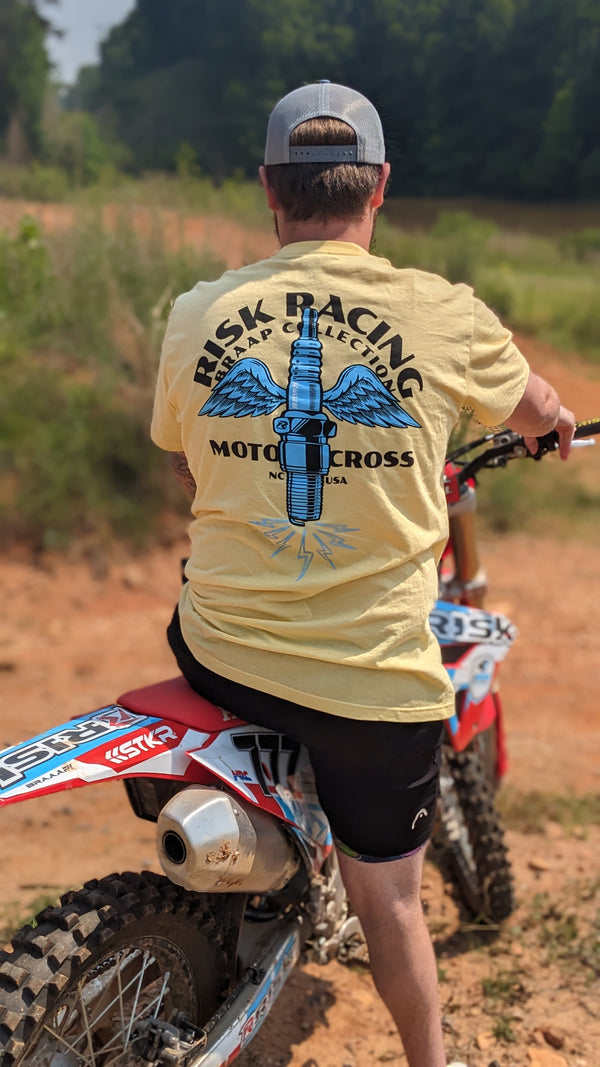Male sitting on a dirt bike with his back to us showing off his yellow spark wings Risk Racing shirt.