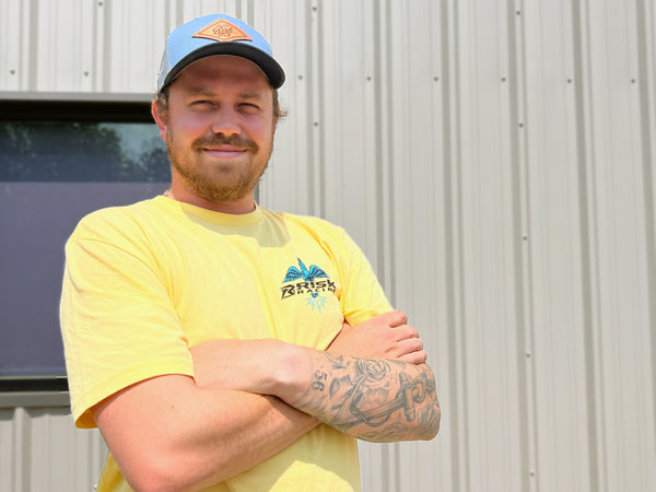 Brad from Risk Racing wearing a yellow 'spark wings' t-shirt and blue patch hat