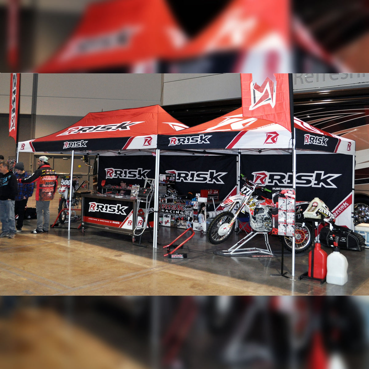 A 10x10 and 10x20 canopy pit tent with tent walls installed on the back wall of both. Showroom floor setting at a trade show.