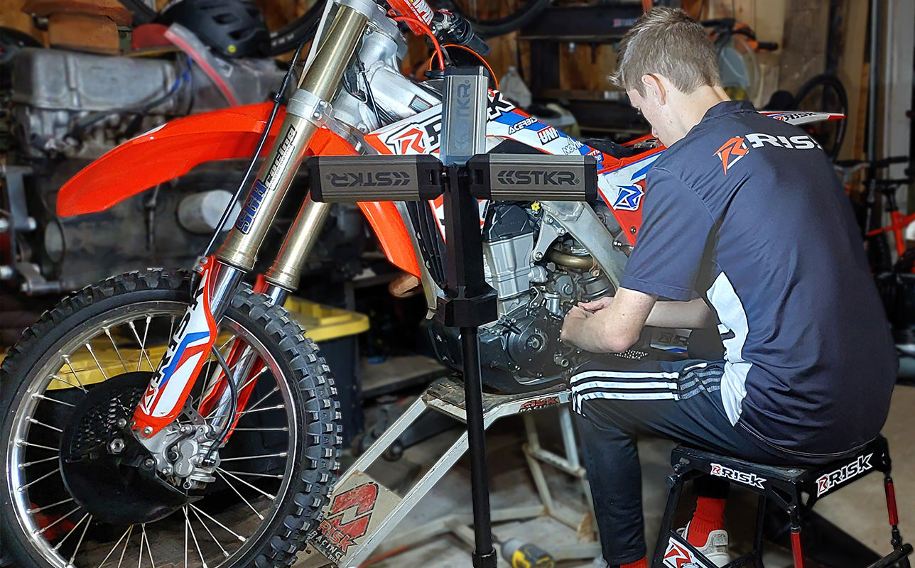 young man working on a dirt bike inside a garage illuminated by an STKR TRi-Mobile area light with tripod