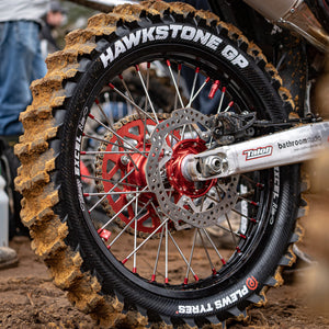 Close up on a dirt bike rear tire and swing arm. Brand new HAWKSTONE GP from Plews Tyres with a clean sidewall and dirty paddles.