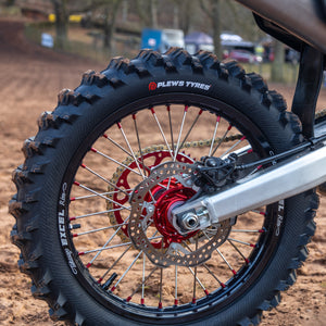 Close up of a Hawkstone paddle tire by plews tyres and swing arm. The dirt bike is sitting on an ATS stand by Risk Racing with a wet MX track in the background.