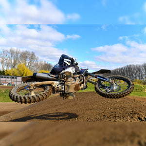 motocross racer whipping super low over a jump and very horizontal. bottom of the bike towards camera really showing us the plews tires.