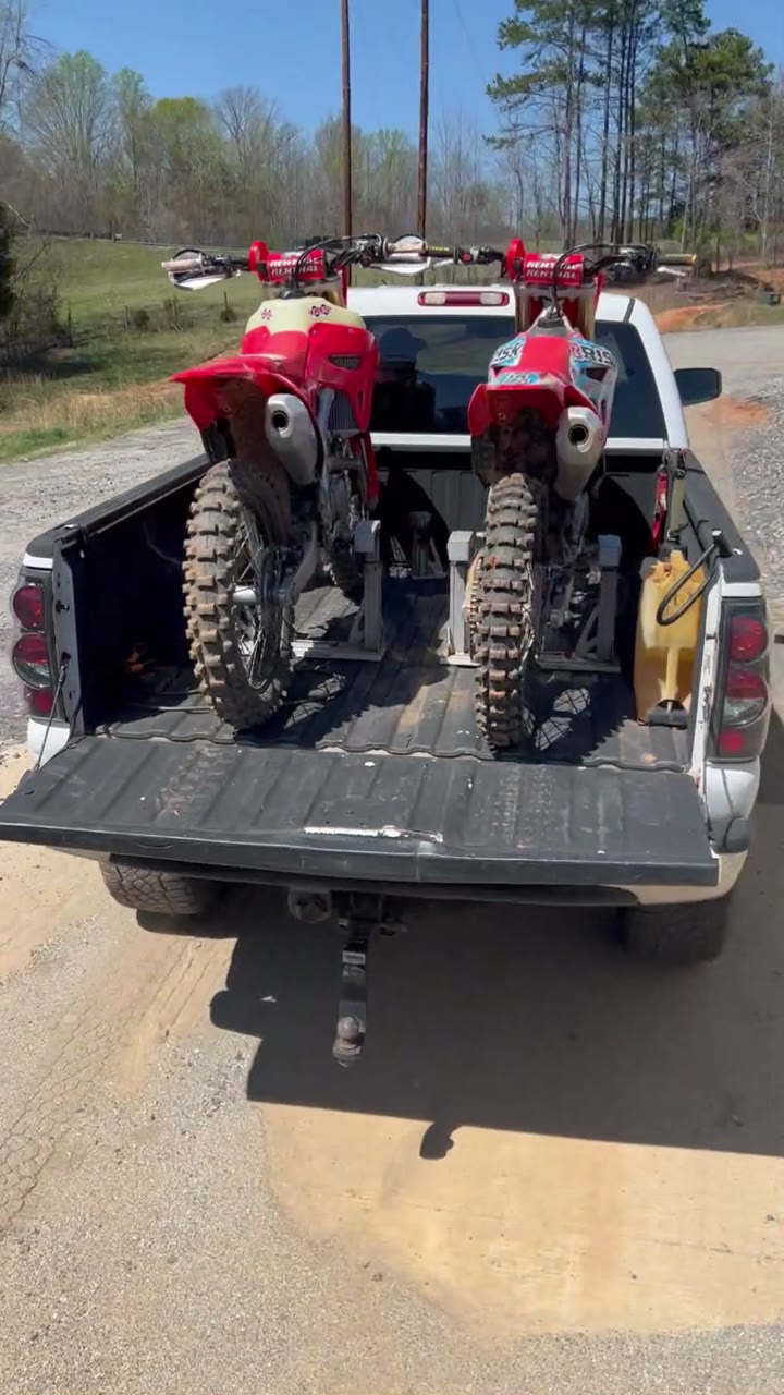 Two dirt bikes side by side in a pickup bed on Lock-N-Load Pro, with no straps and a utility jug beside them